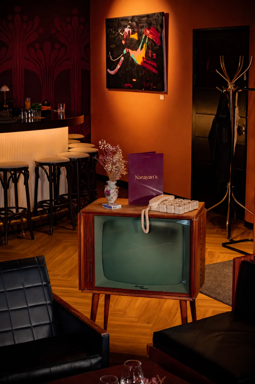 Narayan's lounge corner with artwork, vintage television cabinet, and a Narayan's menu